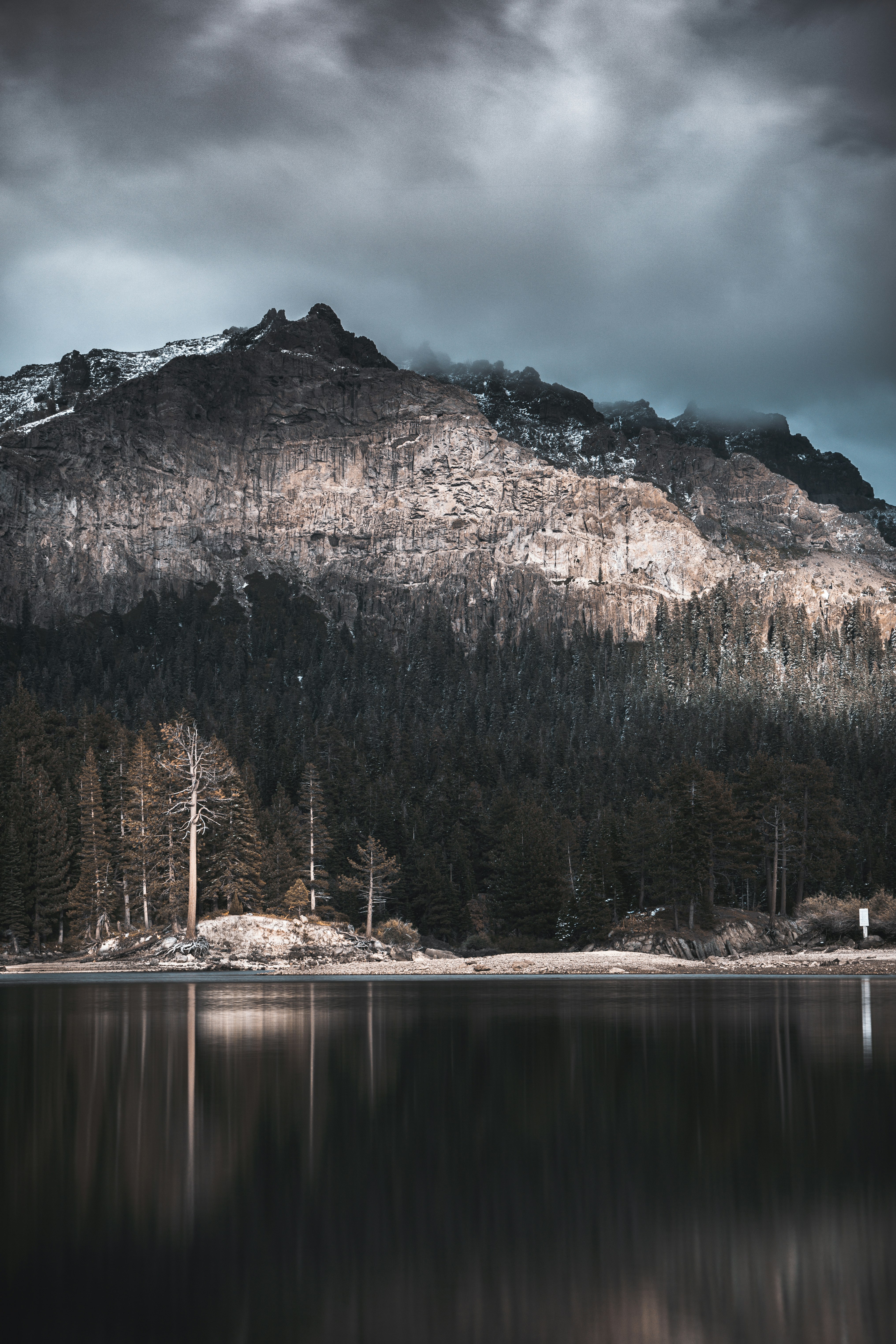 lake by mountain under gray skies at daytime